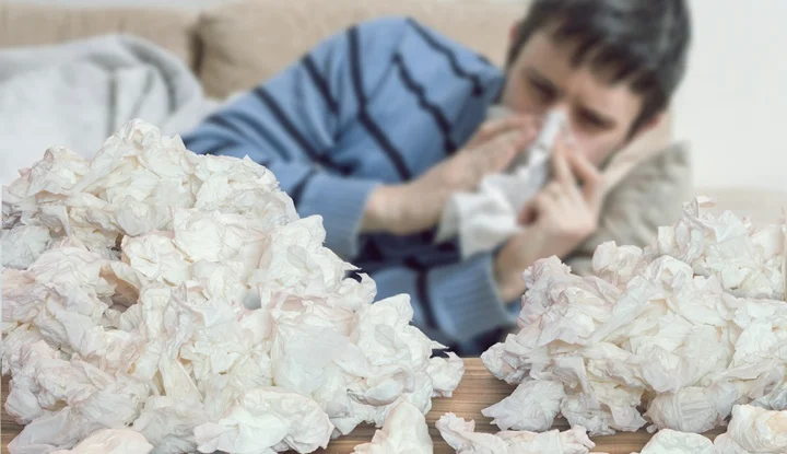 Funny sick man who has flu blowing nose with tissues