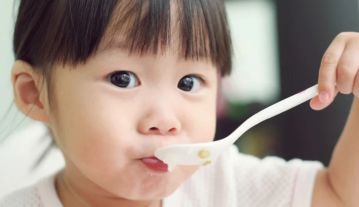 Toddler girl feeding herself porridge