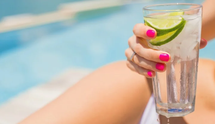 Woman holding refreshing cold drink by the pool