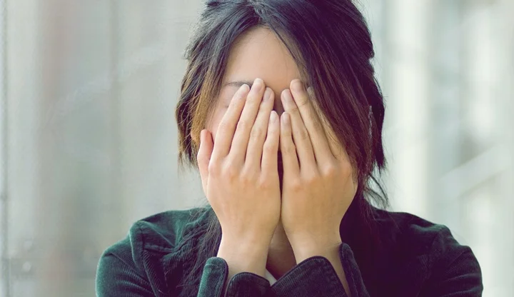 Asian woman covering eyes with her hands.